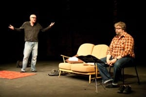 Tim Crouch with an oblivious actor on stage with a script and instructions in front of him.